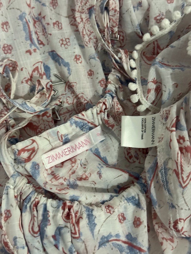 Zimmermann cotton printed tank top size 0 (Category: Sleeveless) located in Cebu City. Submitted by hotchkisscebu (Listing ID 1469643394, Image 2). Description: - Brand: Zimmermann - Material: 100% lightweight and breezy cotton - Design: White base with a vibrant red and blue floral print - Details: Delicate spaghetti straps with hardware adjusters, chic cutout lace trim around the midsection, and playful pom-pom trim along the bottom hem - Size: