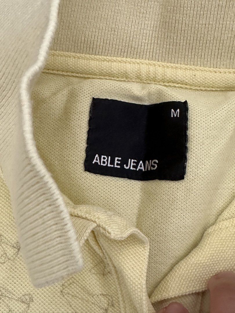 Able Jeans Yellow Graphic Polo Shirt Medium (Category: Tshirts & Polo Shirts ) located in Cainta. Submitted by buy.preloved (Listing ID 1469791122, Image 2). Description: - Brand: Able Jeans - Color: Light yellow - Size: Medium (tag inside collar) - Design: Embroidered 'ABLE JEANS MAKE IT HAPPEN' with detailed bird and feather graphics trailing to the hem - Style: Classic collar, 3-button placket, short sleeves - Condition: Excellent pre-loved co