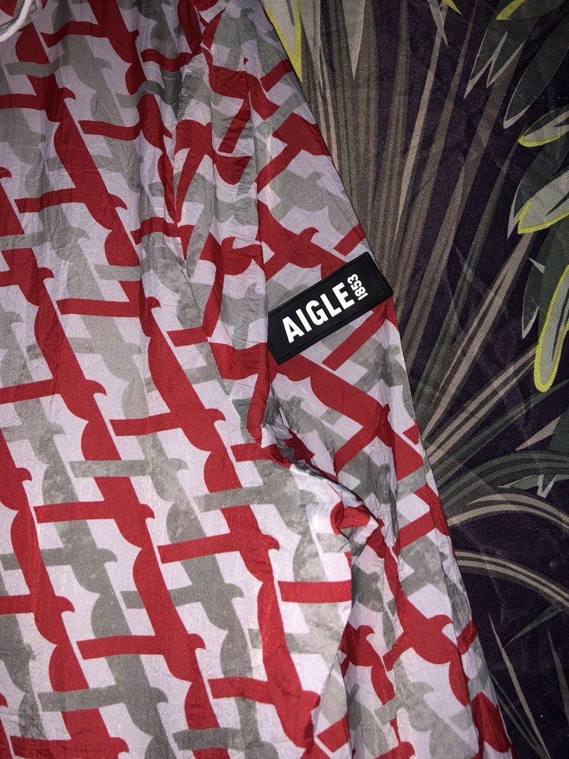 Aigle 1853 Red Grey Patterned Packable Hooded Windbreaker Jacket (Category: Coats, Jackets and Outerwear) located in Bacolod City. Submitted by goodthrifts6121 (Listing ID 1469802126, Image 3). Description: - Brand: Aigle 1853 - Design: Red and grey patterned windbreaker - Feature: Packs down into its own attached zippered pouch - Details: Full zip front, adjustable hood, elastic waist toggles, and zipped side pockets - Branding: Iconic label pat