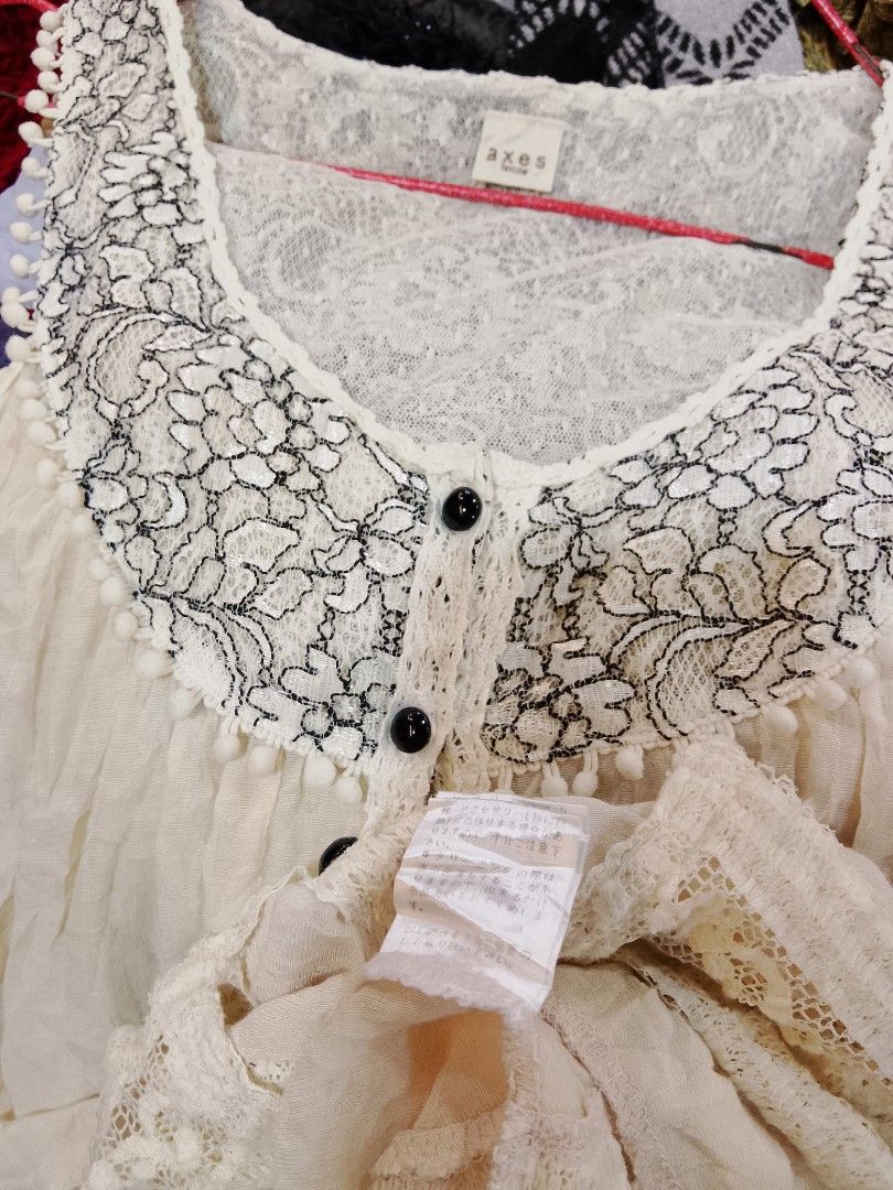 axes femme Lace Collar Button Down Blouse (Category: Blouses) located in Manila. Submitted by keencrystal.595c28 (Listing ID 1469833841, Image 3). Description: Cream sleeveless top from axes femme. Detailed with black floral lace around the neckline, pom-pom trim, and front buttons. Layered lace panels near the hem create an asymmetrical, flowy look. Size tag shows M. Lightweight, breezy material. Great piece for layering or warm weather..