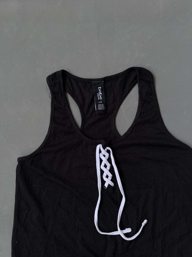 bebe Black Lace-Up Tank Top (Category: Sleeveless) located in Baguio. Submitted by lovelaira (Listing ID 1469852504, Image 3). Description: Black bebe racerback tank top in size L. White lace-up drawstring front with metal grommets. White bebe branding and double stripe detail near the bottom hem. Material is 58% cotton, 37% polyester, 5% spandex. Soft and stretchy sleepwear fabric. Clean tag intact..
