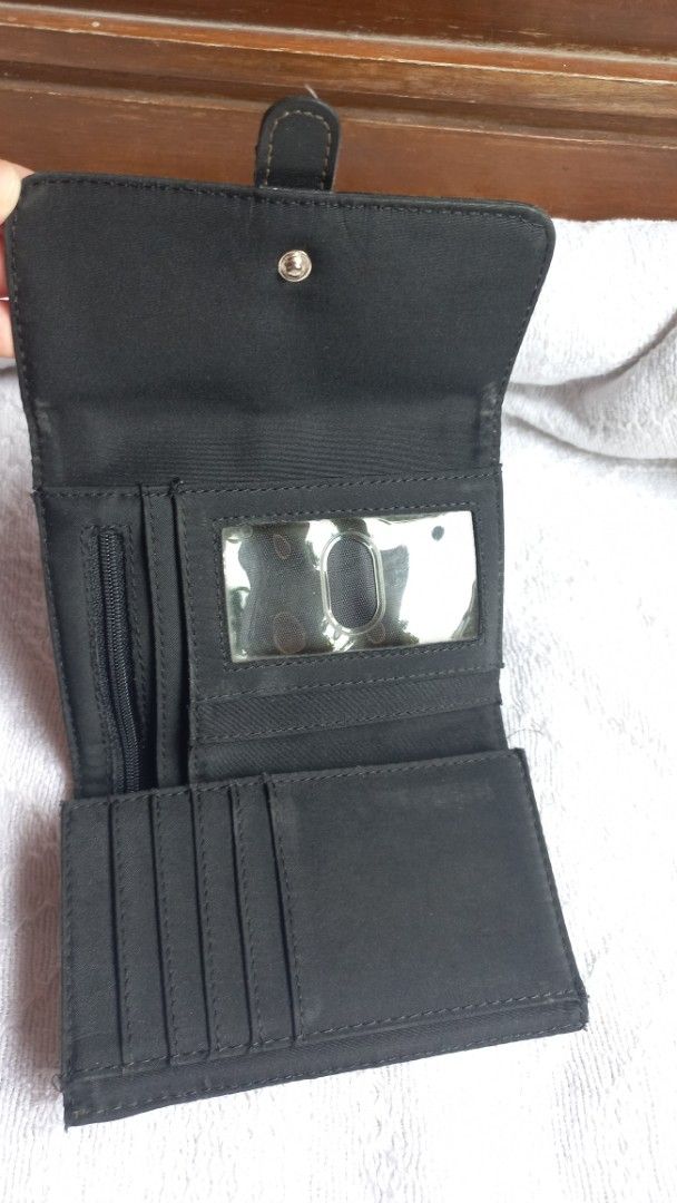 Black patterned trifold wallet with buckle strap (Category: Wallets & Card holders) located in Rizal. Submitted by mayra74 (Listing ID 1469766560, Image 2). Description: - Color: Black - Design: Textured exterior with decorative strap and buckle accent - Closure: Secure magnetic snap - Interior Features: Multiple card slots, clear ID window, slip pockets, and zippered coin compartment - Size: Compact and fits easily into any handbag - Condition: 