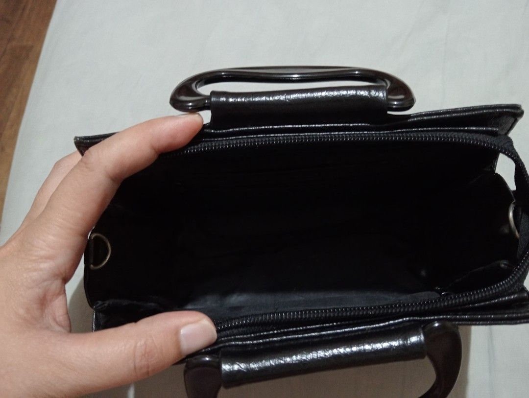 Black Pouchette Handbag with Plastic Handle (Category: Luxury Bags & Wallets) located in Makati City. Submitted by YSL80022 (Listing ID 1469875814, Image 3). Description: - Color & Design: Black structured handbag with debossed logo on the front corner - Material: Premium textured faux leather - Handles: Sturdy, rigid plastic top handles - Closure & Interior: Secure zippered main compartment with clean fabric lining - Structure: Compact rectangul