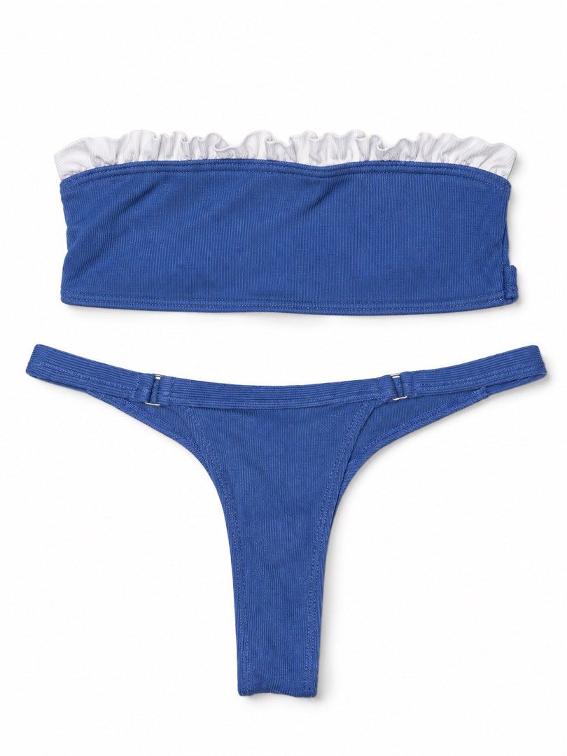 Blue Two-Piece Bikini Set with White Ruffle Detail (Category: Bikinis & Swimsuits) located in Marikina City. Submitted by ziaziaaa (Listing ID 1469891561, Image 2). Description: - Style: Two-piece swimsuit set in a vibrant royal blue - Material: Textured ribbed fabric - Top: Bandeau style with contrasting white ruffled trim on the upper edge - Bottoms: High-cut thong silhouette with thin side straps and adjustable metal hardware sliders - Conditi