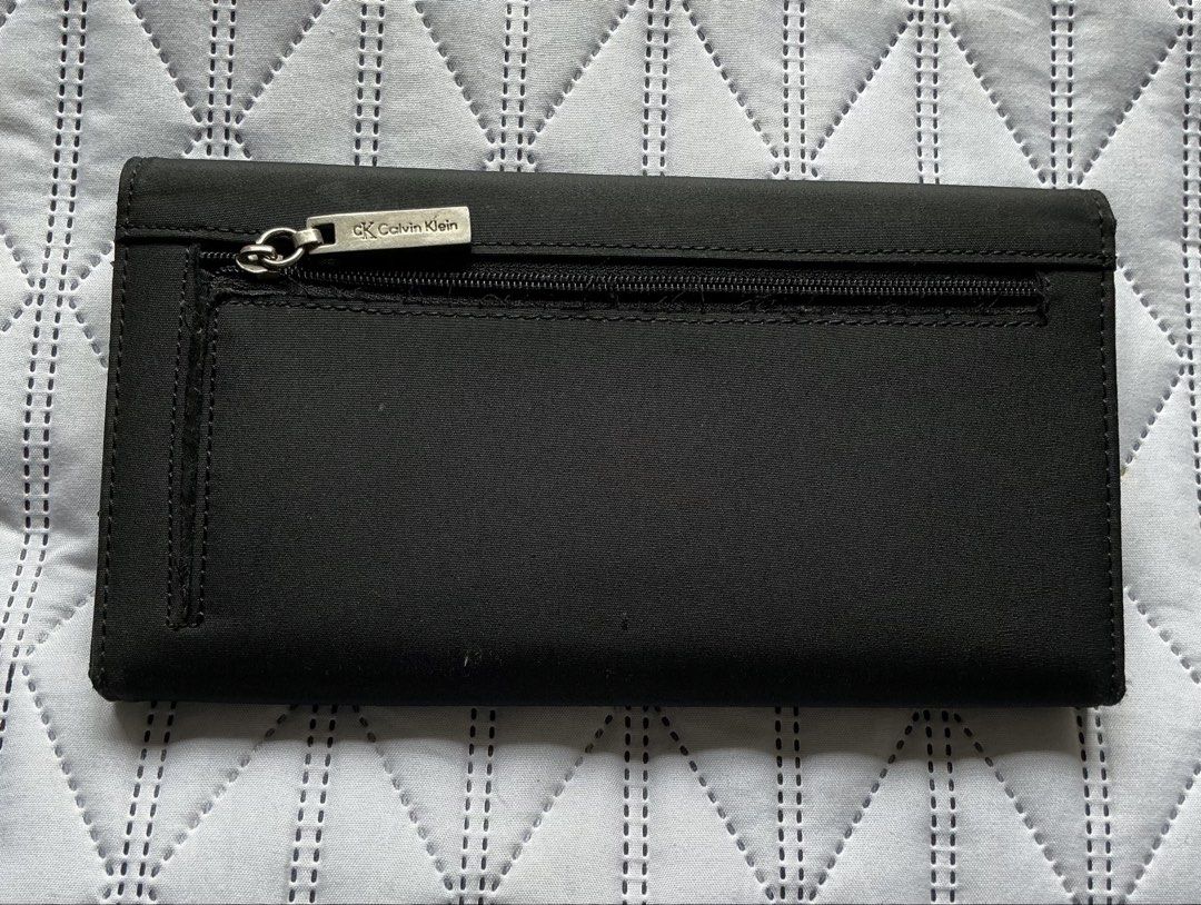 Calvin Klein Long Wallet (Category: Wallets & Card holders) located in Makati City. Submitted by boldturtle-8720 (Listing ID 1469795966, Image 2). Description: Authentic black long flap Calvin Klein wallet featuring a silver metal plaque with the Calvin Klein logo (ck Calvin Klein). Material: woven nylon .