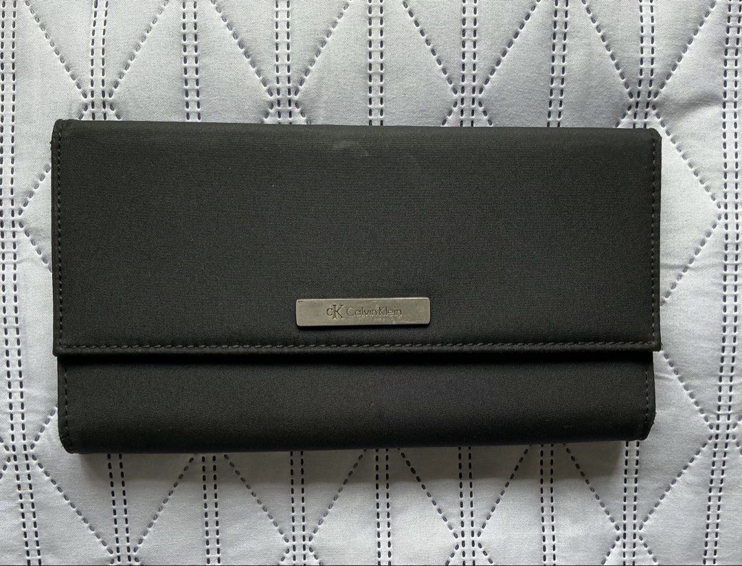 Calvin Klein Long Wallet (Category: Wallets & Card holders) located in Makati City. Submitted by boldturtle-8720 (Listing ID 1469795966, Image 1). Description: Authentic black long flap Calvin Klein wallet featuring a silver metal plaque with the Calvin Klein logo (ck Calvin Klein). Material: woven nylon .