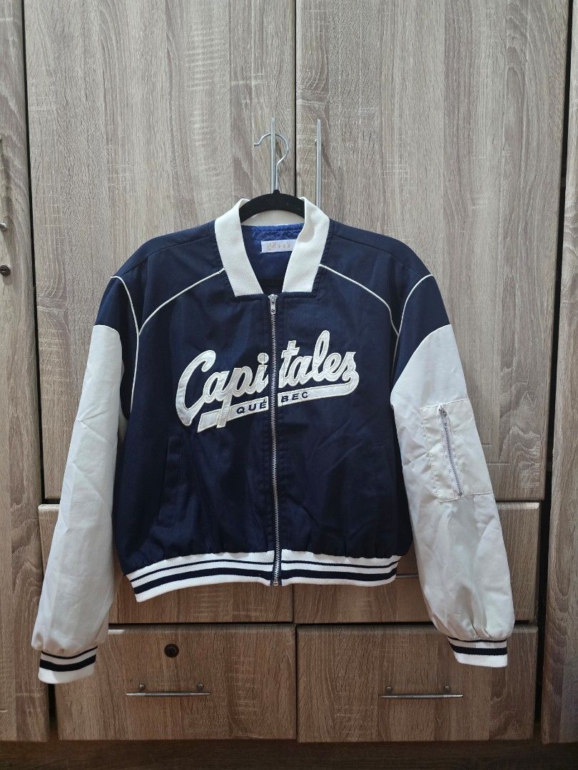 Capitales Quebec Blue and White Bomber Jacket (Category: Coats, Jackets and Outerwear) located in Manila. Submitted by cee_gotaway6991 (Listing ID 1469825414, Image 1). Description: - Style: Navy blue and white varsity jacket with zipper closure - Design: Capitales Quebec embroidered lettering across the chest - Details: Striped ribbed cuffs and hem, plus an extra zipped utility pocket on the left sleeve - Material: Lightweight fabric - Status: R