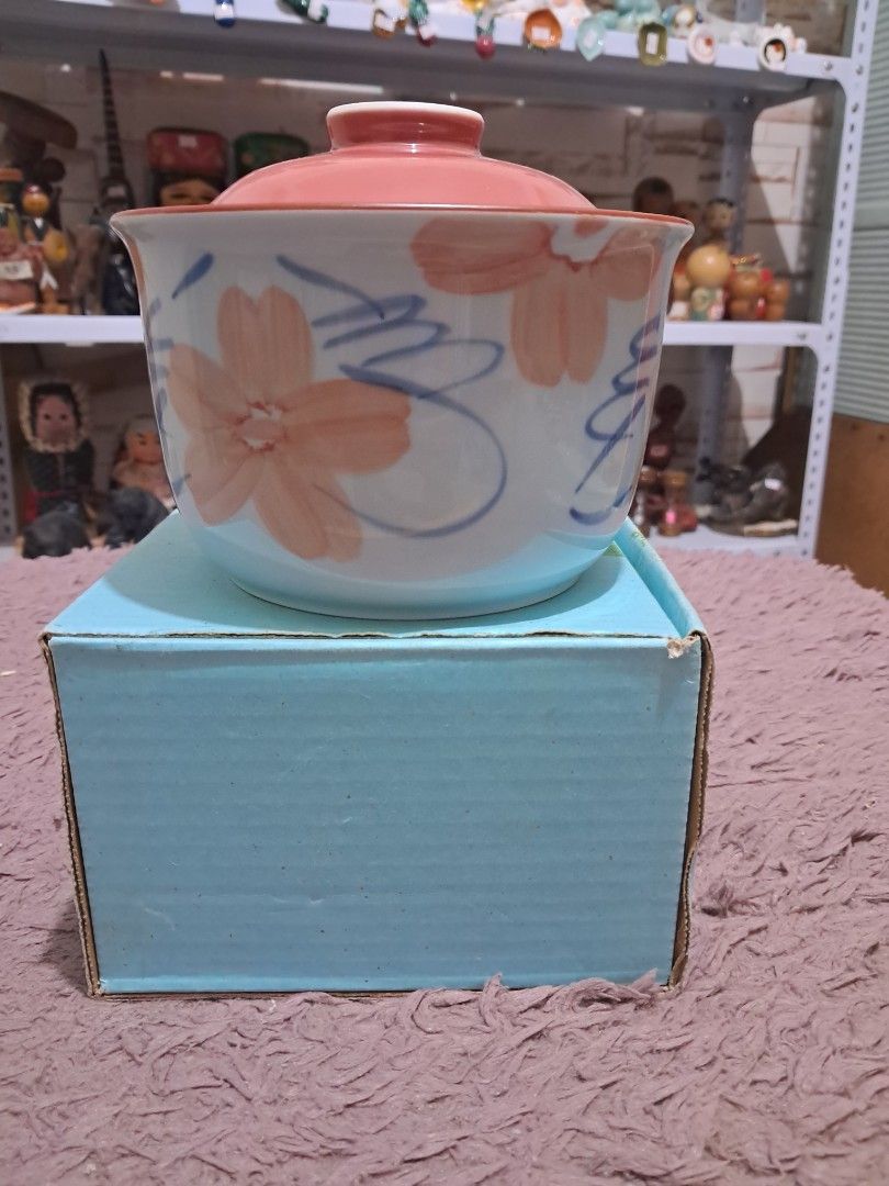 Ceramic bowl (Category: Dinnerware & Cutlery) located in Cavite. Submitted by secretjapansurplus (Listing ID 1469904962, Image 1). Description: This is a Japanese-style lidded ceramic bowl on its original blue box, used to serve hot soups, stews, or steamed eggs (chawanmushi). • Bowl Design: Features hand-painted peach/pink cherry blossoms with fine blue vine accents on a white glazed porcelain body. • Lid Design: Features a solid matching pink d
