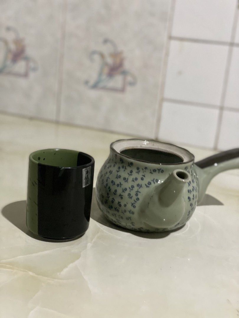 Ceramic Teapot with Matching Cup Set (Category: Coffee & Tea Tableware) located in Manila. Submitted by geminibibo (Listing ID 1469862015, Image 1). Description: - Green ceramic teapot featuring a delicate blue floral pattern and unique side-handle design - Includes a tall matching cup with a sleek black exterior and green interior - Perfect solo tea set for one person - Clean interior, ready for immediate brewing - Pre-loved and well-maintained 