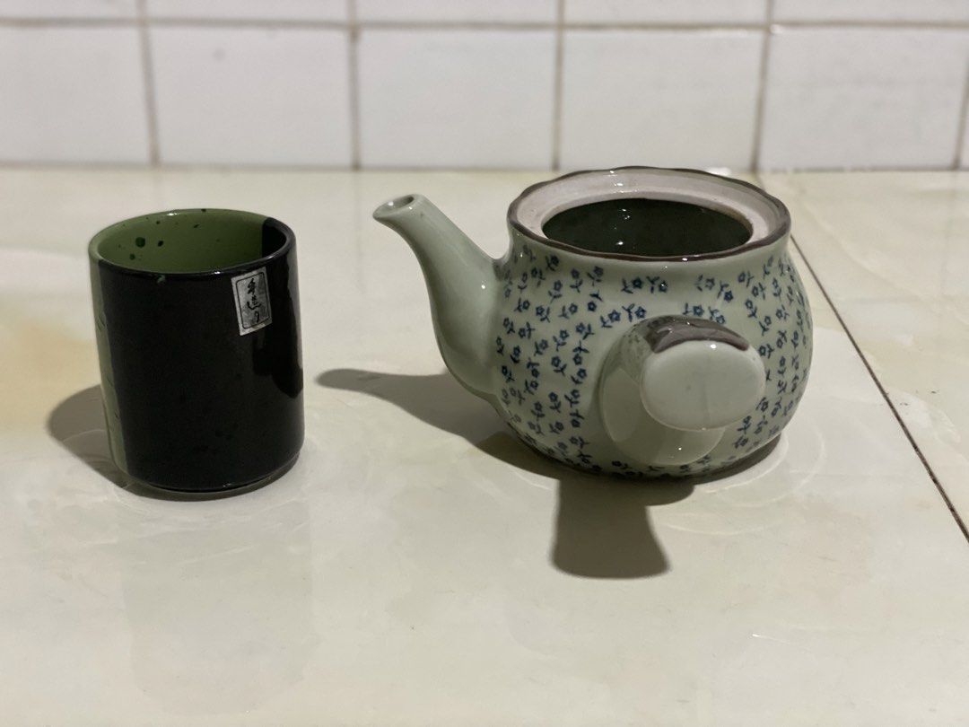 Ceramic Teapot with Matching Cup Set (Category: Coffee & Tea Tableware) located in Manila. Submitted by geminibibo (Listing ID 1469862015, Image 3). Description: - Green ceramic teapot featuring a delicate blue floral pattern and unique side-handle design - Includes a tall matching cup with a sleek black exterior and green interior - Perfect solo tea set for one person - Clean interior, ready for immediate brewing - Pre-loved and well-maintained 