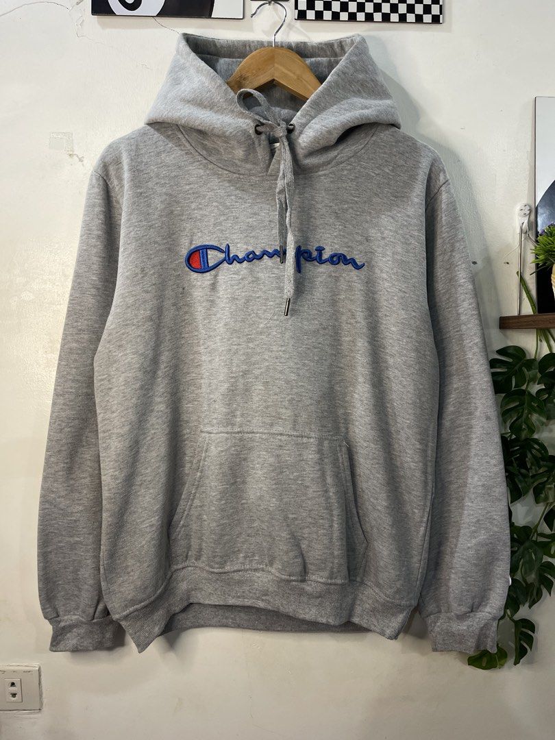 Champion Grey Script Logo Hoodie XX-Large (Category: Hoodies) located in Cabagan. Submitted by blessingma81004 (Listing ID 1469767471, Image 2). Description: - Brand: Champion - Color: Grey with embroidered blue script logo - Features: Kangaroo front pocket, adjustable drawstring hood - Size: Tagged XX-Large (fits like a Medium-Large based on measurements).