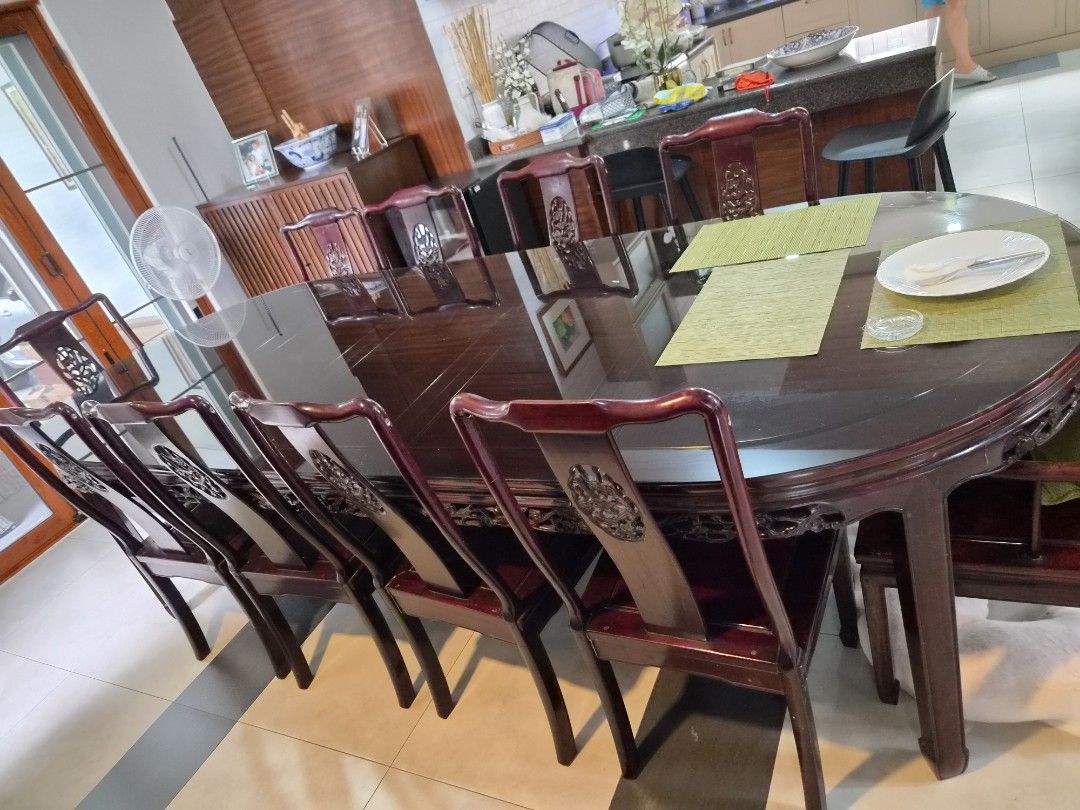 Chinese Rosewood Dining Table with chairs (Category: Tables & Sets) located in Paranaque City. Submitted by angela2002 (Listing ID 1469779164, Image 2). Description: - Chinese Rosewood Dining Table with chairs - Elegant dark wood dining set with a rich reddish-brown finish - Large table featuring a protective oval glass top overlay - Includes matching wooden armchairs with stylish carved circular backrests - Solid, heavy construction built to las