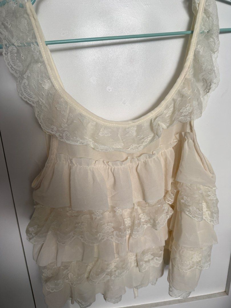 Cream Lace Ruffle Layered Sleeveless Top (Category: Sleeveless) located in Pasig City. Submitted by atbp__ (Listing ID 1469810009, Image 3). Description: - Cream layered camisole with sweet ruffle and lace details best fits small - Scoop neckline featuring front ribbon ties and small functional buttons - Super soft, lightweight, and breathable fabric - Perfect for layering or as a standalone top on warm days - Clean condition with no obvious flaw