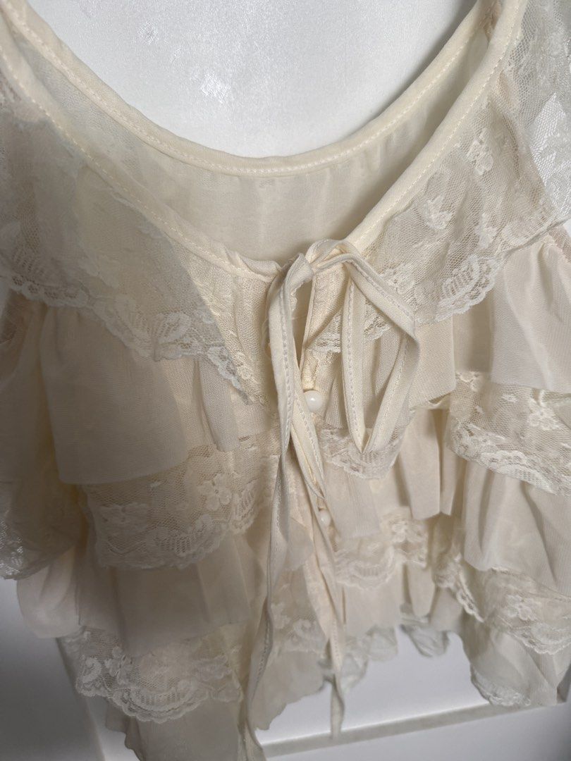 Cream Lace Ruffle Layered Sleeveless Top (Category: Sleeveless) located in Pasig City. Submitted by atbp__ (Listing ID 1469810009, Image 2). Description: - Cream layered camisole with sweet ruffle and lace details best fits small - Scoop neckline featuring front ribbon ties and small functional buttons - Super soft, lightweight, and breathable fabric - Perfect for layering or as a standalone top on warm days - Clean condition with no obvious flaw