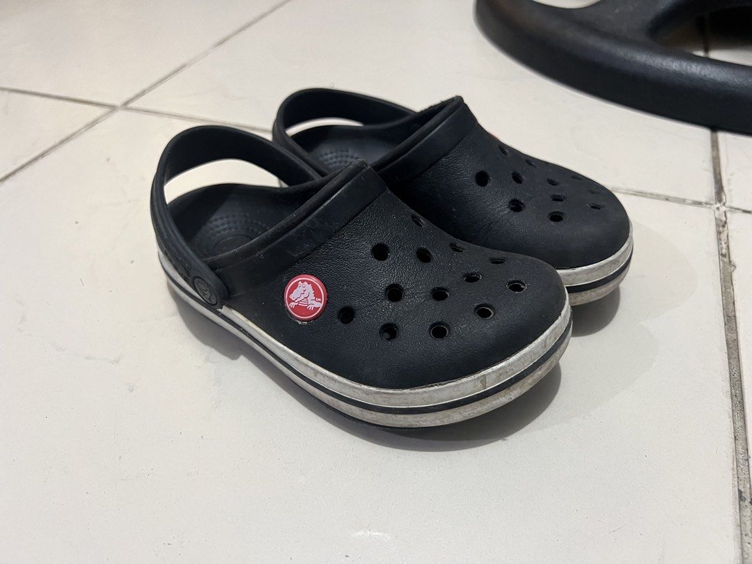 Crocs Black Clogs Shoes Size 10-11 (Category: Babies & Kids Fashion) located in Cavite. Submitted by nlp_preloved (Listing ID 1469910154, Image 1). Description: - Color: Classic black with white stripe and red logo button - Style: Slip-on with a secure back strap - Size: Marked as 10-11 (Made in Argentina) - Condition: Normal signs of wear on the bottom tread - Ideal for casual, everyday wear.