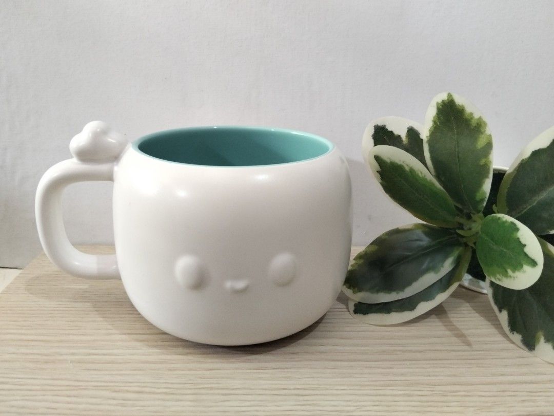 Cute White and Turquoise Ceramic Mug with Face (Category: Coffee & Tea Tableware) located in Caloocan City. Submitted by agr_shop (Listing ID 1469833089, Image 1). Description: - Material: Sturdy ceramic with matte white finish - Interior: Vibrant turquoise - Design: Minimalist embossed sleepy face with a cloud detail on the handle - Use: Great size for morning coffee or tea.