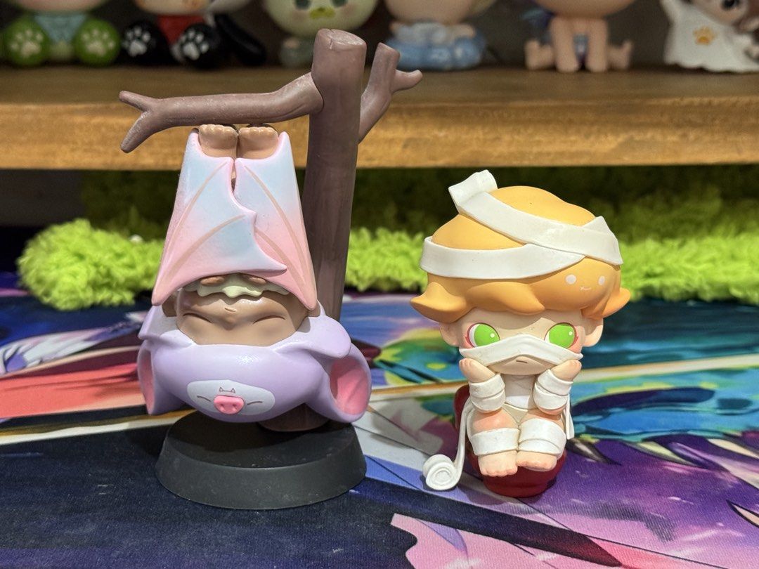 Dimoo Blind Box Designer Figures Bat and Mummy Characters (Category: Designer & Blind Box Toys) located in Calamba. Submitted by blissblixi12029 (Listing ID 1469887022, Image 1). Description: - Set of 2 cute blind box collectible figures - Figure 1: Character in a pinkish-blue bat costume hanging upside down from a branch - Figure 2: Mummy character with bright green eyes on a small red base - High-quality, detailed painting and fun character des