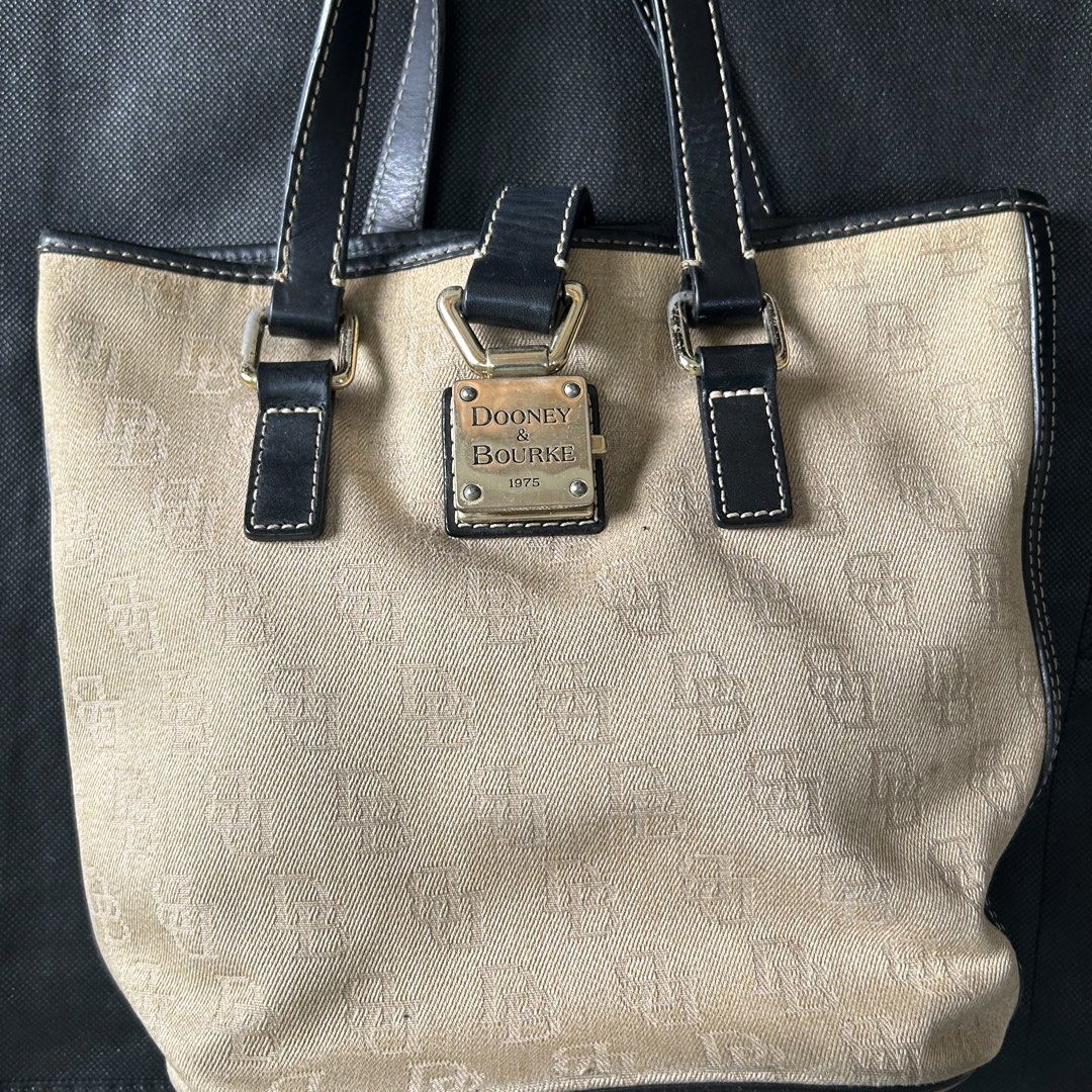 Dooney & Bourke Monogram Canvas Tote Bag (Category: Luxury Bags & Wallets) located in Makati City. Submitted by declutter__queen (Listing ID 1469783023, Image 3). Description: - Brand: Dooney & Bourke - Style: Signature monogram canvas tote bag in neutral beige - Straps: Dark leather with stylish white contrast stitching and double handles for shoulder carry - Details: Front metal padlock featuring the brand name and 1975 founding year - Interior