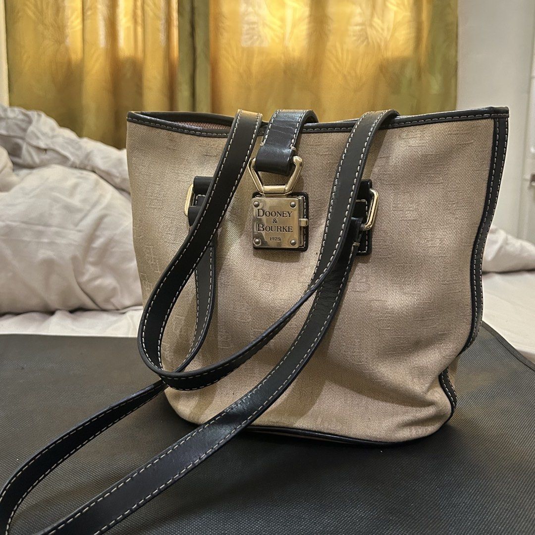 Dooney & Bourke Monogram Canvas Tote Bag (Category: Luxury Bags & Wallets) located in Makati City. Submitted by declutter__queen (Listing ID 1469783023, Image 1). Description: - Brand: Dooney & Bourke - Style: Signature monogram canvas tote bag in neutral beige - Straps: Dark leather with stylish white contrast stitching and double handles for shoulder carry - Details: Front metal padlock featuring the brand name and 1975 founding year - Interior