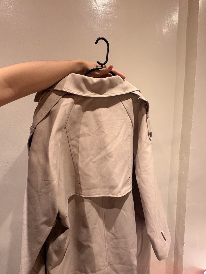 Double-Breasted Trench Coat Outerwear (Category: Coats, Jackets and Outerwear) located in Caloocan City. Submitted by celest.xxx (Listing ID 1469856647, Image 2). Description: - Brand: FOCUS.S - Color: Clean neutral beige - Design: Double-breasted front with dark tortoiseshell buttons - Features: Wide lapel collar, front pockets, smooth white inner lining, and back storm flap overlay - Sleeves: Long sleeves with adjustable button strap detail nea