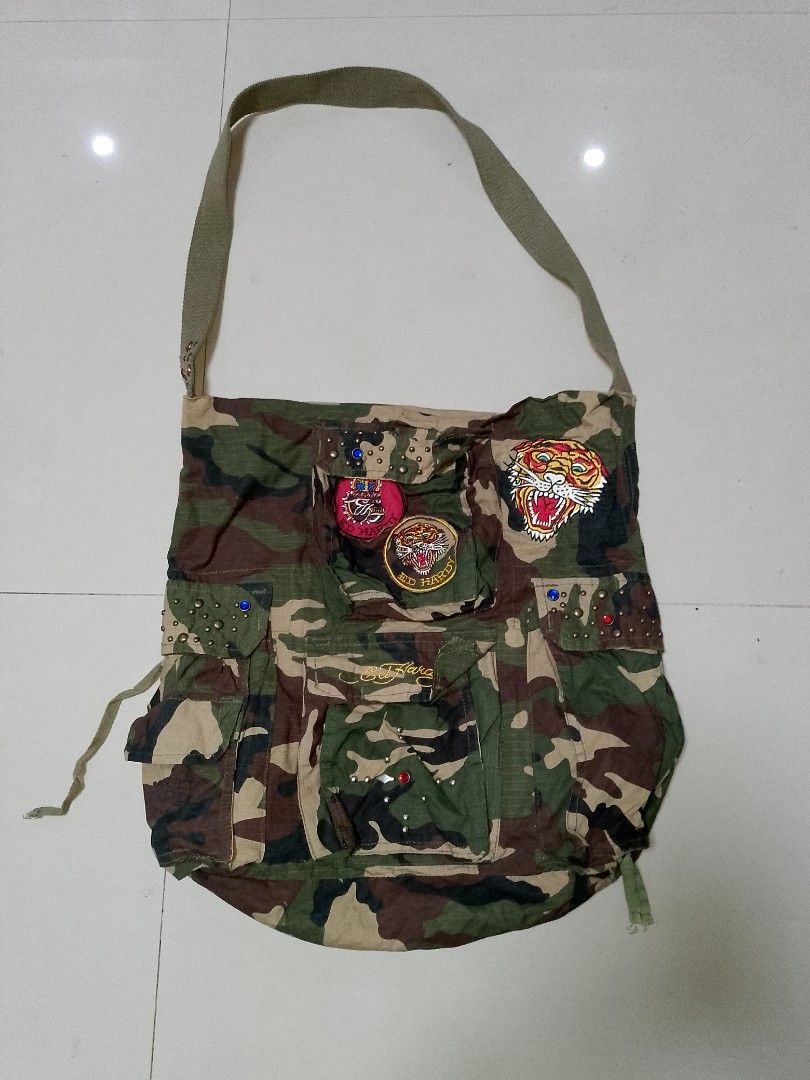 Ed Hardy Camo Shoulder Bag with Patches and Studs (Category: Shoulder Bags) located in Manila. Submitted by mjthrifted_second (Listing ID 1469820530, Image 1). Description: Green camouflage canvas shoulder bag by Ed Hardy. Multiple front pockets with button flaps, metal studs, and colorful rhinestone accents. Embroidered tiger patches and Ed Hardy script logo on the front. Adjustable strap and fabric lining inside. Casual everyday carryall with p
