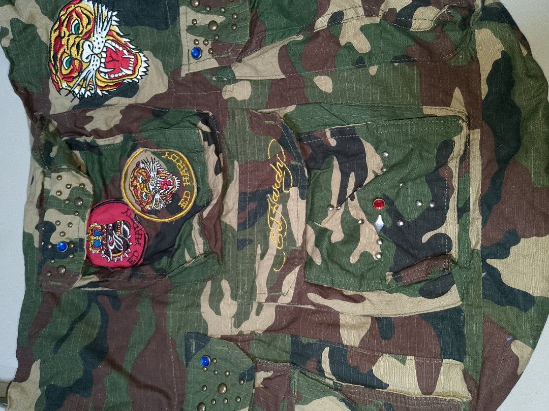 Ed Hardy Camo Shoulder Bag with Patches and Studs (Category: Shoulder Bags) located in Manila. Submitted by mjthrifted_second (Listing ID 1469820530, Image 3). Description: Green camouflage canvas shoulder bag by Ed Hardy. Multiple front pockets with button flaps, metal studs, and colorful rhinestone accents. Embroidered tiger patches and Ed Hardy script logo on the front. Adjustable strap and fabric lining inside. Casual everyday carryall with p