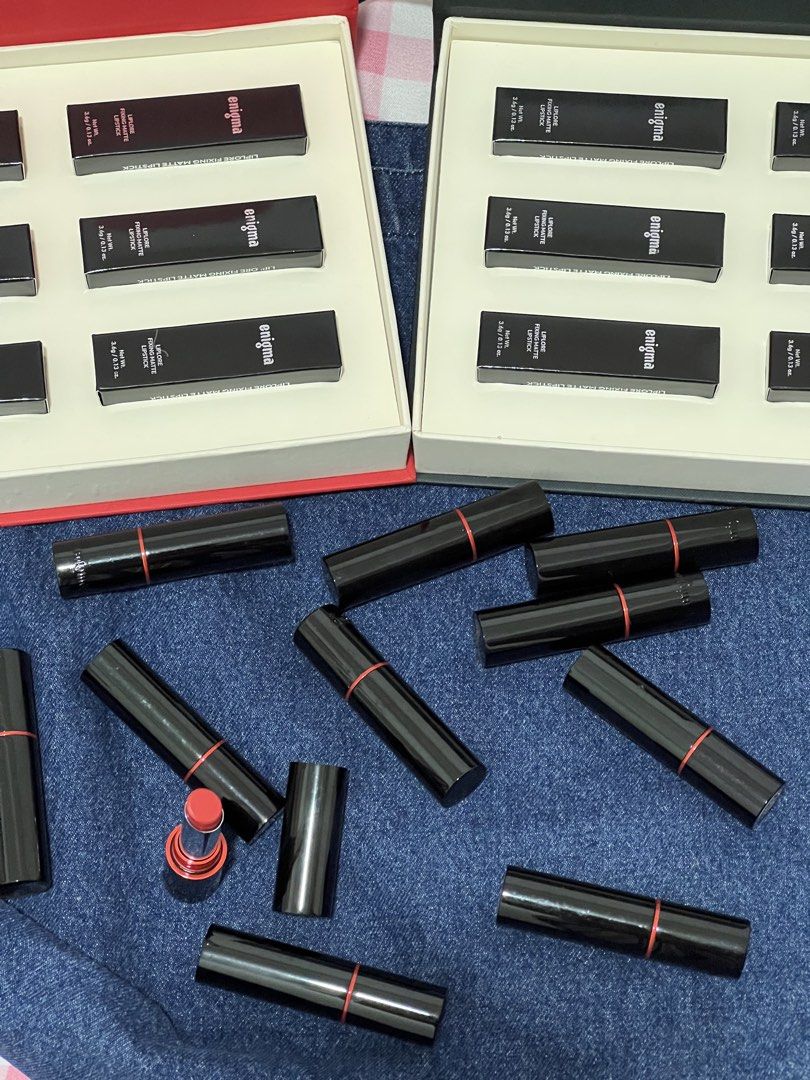 Enigma Liplore Fixing Matte Lipstick Set (Category: Makeup) located in Manila. Submitted by andeng30 (Listing ID 1469872119, Image 2). Description: - Brand: Enigma Liplore - Type: Fixing Matte Lipstick Collection - Bundle includes: 2 full presentation boxes with boxed lipsticks and multiple loose tubes - Shade shown: Vibrant coral-red (one tube uncapped) - Packaging: Heavy black tubes featuring a chic red ring detail on the caps - Condition: Bran