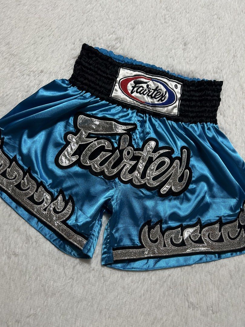 Fairtex Blue Silver Muay Thai Shorts Size M (Category: Shorts) located in Quezon City. Submitted by commonwealthpickerph (Listing ID 1469801176, Image 2). Description: - Brand: Fairtex - Style: Muay Thai shorts in bright blue satin - Details: Silver textured script logo and matching silver flame trim - Waistband: Thick black elastic with classic oval brand patch - Size: Medium (tag inside) - Material: 100% polyester, made in Thailand - Condition: