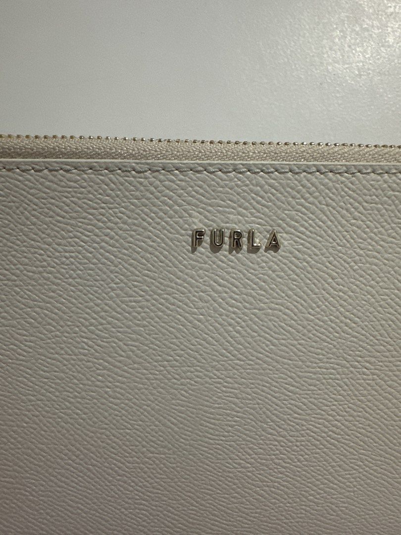 Furla Genuine Leather Wristlet (Category: Luxury Bags & Wallets) located in Cainta. Submitted by xyzasisa (Listing ID 1469946786, Image 2). Description: - Authentic Furla beige pouch in textured Saffiano-style leather - Comes with a convenient wrist strap for easy carrying - Secure zipper closure with elegant gold hardware - Clean fabric-lined interior featuring the genuine Furla leather tag - Slim profile, ideal for holding daily essentials - Sh