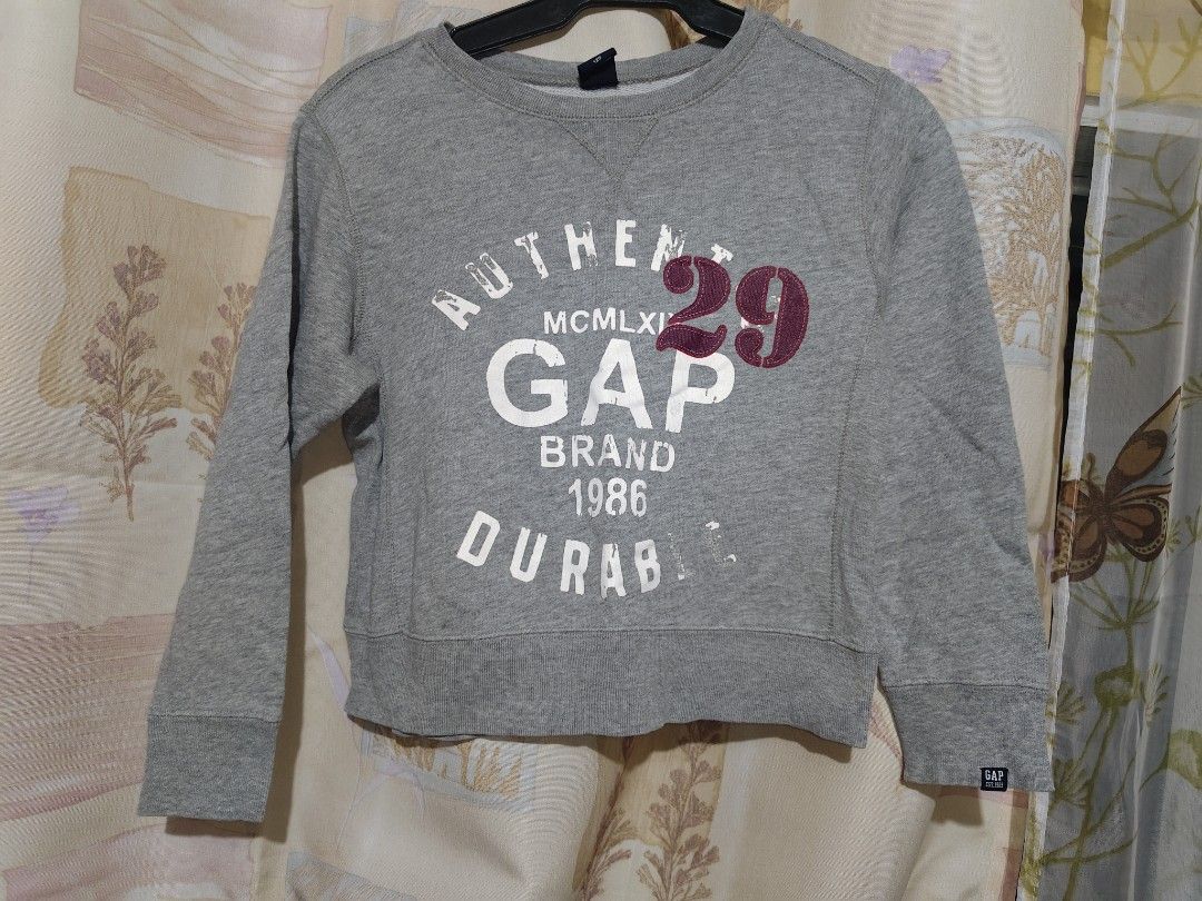 Gap Kids Grey Graphic Sweatshirt Size 120 (Category: Babies & Kids Fashion) located in Manila. Submitted by duffy-080 (Listing ID 1469900558, Image 1). Description: Grey Gap Kids sweatshirt with long sleeves and ribbed cuffs. Graphic print on the front with "AUTHENTIC GAP BRAND 1986 DURABLE" and a red appliqued number 29. Small Gap tag on the bottom left hem. Size 120 label at the neckline. Plain solid grey back..