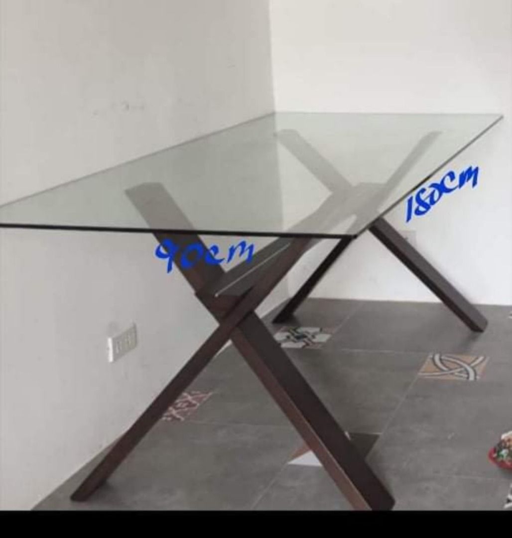 Glass Dining Table with Dark Wood X-Frame Legs (Category: Tables & Sets) located in Cavite. Submitted by jldaaca (Listing ID 1469878104, Image 1). Description: - Type: Glass top dining table - Dimensions: 180cm (L) x 90cm (W) - Design: Modern style with dark brown wooden X-shaped legs - Capacity: Comfortably seats up to 6 people - Condition: Sturdy construction, clean glass surface, with minor signs of use on the frame.