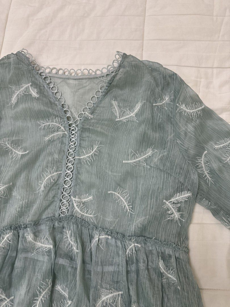 Green Feather Sheer Embroidered Dress (Category: Dresses) located in Quezon City. Submitted by m3gan8 (Listing ID 1469788120, Image 2). Description: - Color: Sage green with white embroidered feather pattern - Material: Lightweight, comfortable fabric - Design: V-neckline with lace trim, half sleeves with circular cutouts - Silhouette: Empire waist, relaxed fit, and flowy tiered hemline - Length: Midi length - Condition: Brand new / Excellent.