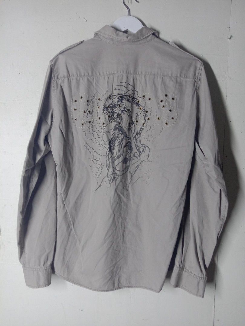 Guess Grey Long Sleeve Button Down Shirt with Back Graphic (Category: Longsleeves) located in Talavera. Submitted by jake_thrift (Listing ID 1469894435, Image 2). Description: - Brand: Guess - Color: Light grey - Style: Long sleeve button-down shirt with classic collar and front placket - Details: Double chest pockets with flap closures, shoulder epaulets - Unique Feature: Eye-catching cat graphic on the back panel surrounded by metal grommet acc