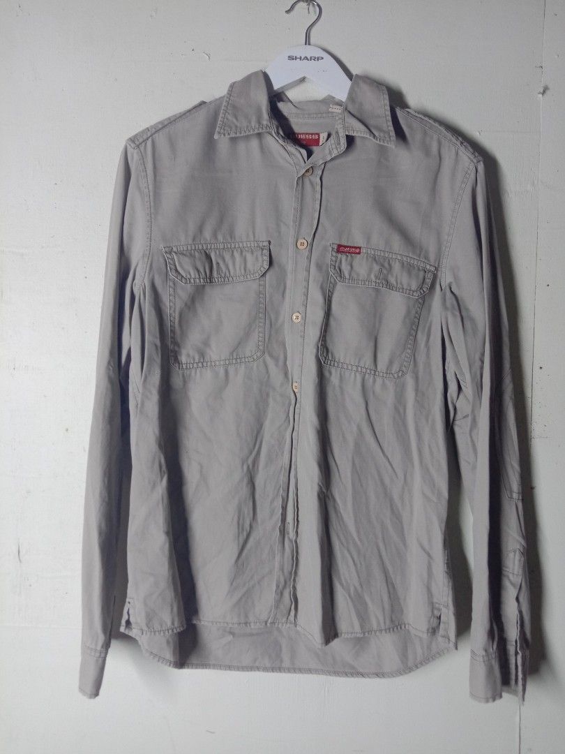Guess Grey Long Sleeve Button Down Shirt with Back Graphic (Category: Longsleeves) located in Talavera. Submitted by jake_thrift (Listing ID 1469894435, Image 1). Description: - Brand: Guess - Color: Light grey - Style: Long sleeve button-down shirt with classic collar and front placket - Details: Double chest pockets with flap closures, shoulder epaulets - Unique Feature: Eye-catching cat graphic on the back panel surrounded by metal grommet acc