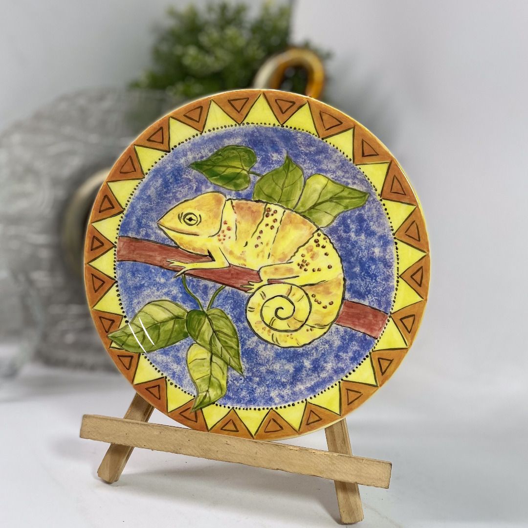 Handpainted Chameleon Ceramic Plate Durban 1997 101426-059 (Category: Dinnerware & Cutlery) located in Quezon City. Submitted by madiscollectibles (Listing ID 1469795187, Image 1). Description: With crazing at the back - Handpainted South African ceramic decorative plate - Features a striking yellow chameleon on a branch with green leaves - Textured blue background with geometric orange and yellow border patterns - Back signed by artist SH (Durba