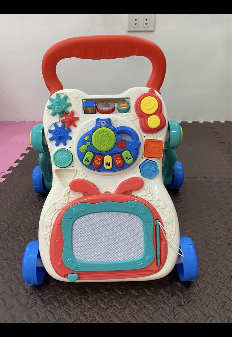 Interactive Multi-Activity Baby Walker with Drawing Board and Toys (Category: Infant Playtime) located in Manila. Submitted by almondchi05 (Listing ID 1469830054, Image 1). Description: All-in-one baby walker and interactive learning center featuring piano keys, gears, shapes, a phone toy, and a built-in erasable drawing board. Designed with a stable four-wheel base and sturdy handle to safely support your toddler's first steps..