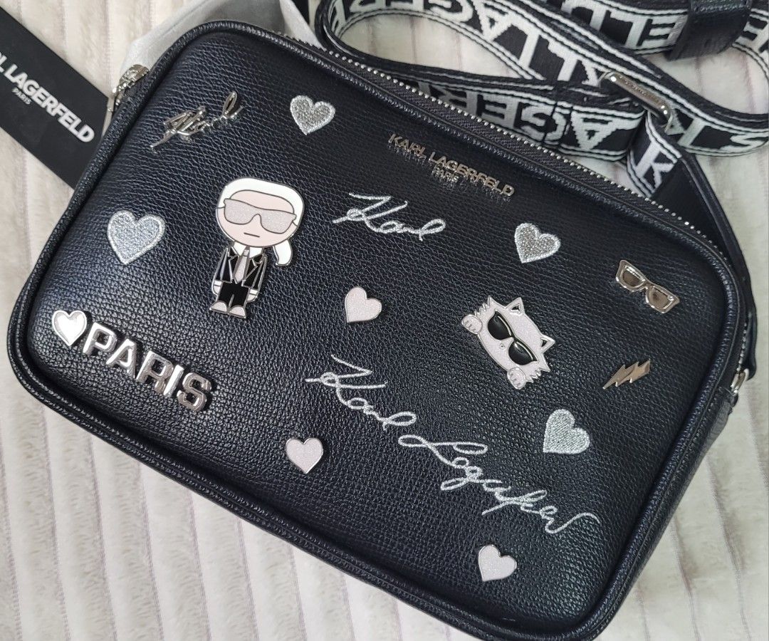 Karl Lagerfeld Paris Black Leather Camera Bag (Category: Cross-body Bags) located in Bocaue. Submitted by thewardrobehub (Listing ID 1469942893, Image 1). Description: 100% authentic and brand new!! Black pebble leather camera bag covered in silver patches, pins, and signatures. Karl Lagerfeld character graphic and Choupette cat face on the front. Double zip top closure with black and white logo webbing strap. It comes with Karl Lagerfeld dust ba