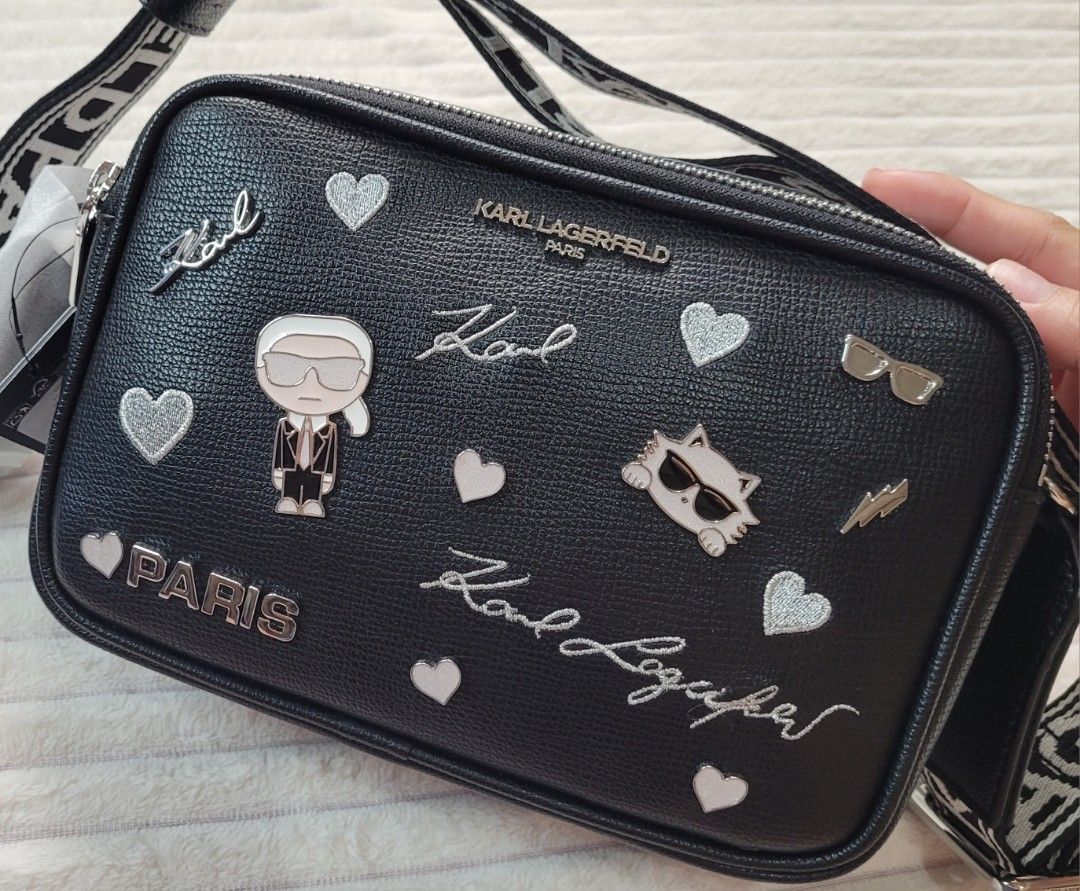 Karl Lagerfeld Paris Black Leather Camera Bag (Category: Cross-body Bags) located in Bocaue. Submitted by thewardrobehub (Listing ID 1469942893, Image 2). Description: 100% authentic and brand new!! Black pebble leather camera bag covered in silver patches, pins, and signatures. Karl Lagerfeld character graphic and Choupette cat face on the front. Double zip top closure with black and white logo webbing strap. It comes with Karl Lagerfeld dust ba