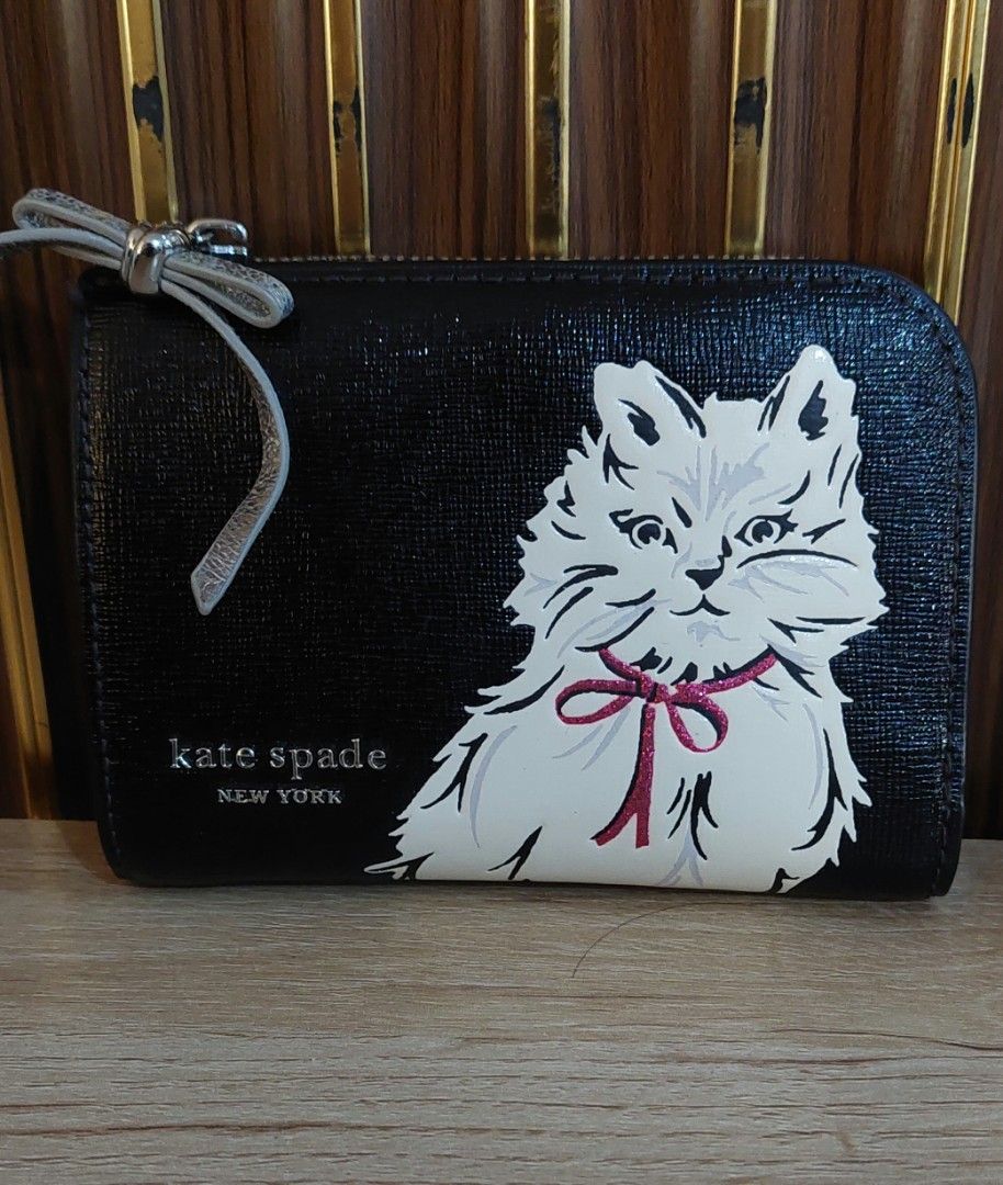 Kate Spade New York Cat Print Wallet (Category: Wallets & Card holders) located in Taguig. Submitted by thrifthub.ph (Listing ID 1469780669, Image 1). Description: - Brand: Kate Spade New York - Material: Genuine black leather - Design: White Persian cat graphic with metallic pink glitter bow - Hardware: Silver-tone with metallic bow zipper pull - Interior: Signature logo lining, multiple card slots, and top zipped coin compartment - Size: Compac