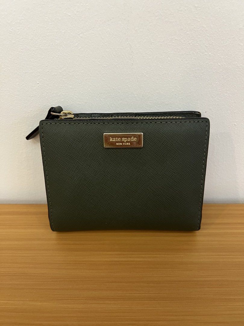 Kate Spade Saffiano Leather Compact Bifold Wallet (Category: Wallets & Card holders) located in Manila. Submitted by pearlt455 (Listing ID 1469770278, Image 1). Description: - Brand: Kate Spade - Color: Dark Green - Material: Textured Saffiano leather - Hardware: Gold tone with metal logo plate - Closure: Secure snap button - Compartments: Multiple card slots and a convenient side zip pocket for coins - Size: Compact, fits easily into mini bags a