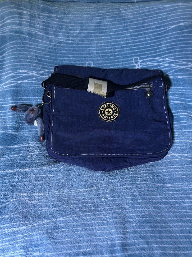 Kipling Blue Messenger Bag With Monkey Keychain (Category: Cross-body Bags) located in Quezon City. Submitted by thriftxgoods (Listing ID 1469897300, Image 1). Description: - Authentic Kipling crossbody/messenger bag in classic navy blue - Features flap closure, adjustable strap, and stylish contrast stitching - Includes the signature fuzzy monkey keychain charm - Spacious main compartment plus a convenient zippered front flap pocket - Clean inte