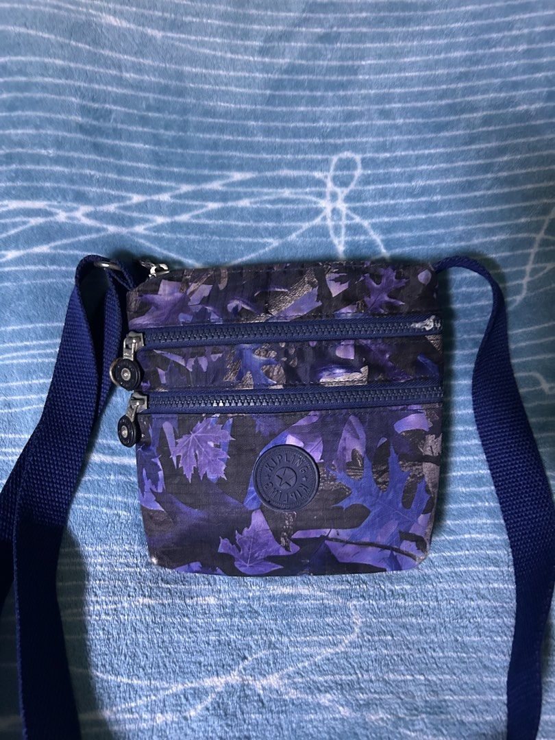 Kipling Purple Leaf Camo Crossbody Bag (Category: Cross-body Bags) located in Quezon City. Submitted by thriftxgoods (Listing ID 1469895661, Image 2). Description: - Design: Purple leaf camo pattern on durable nylon with a blue adjustable strap - Storage: Main zip compartment, 2 zippered front pockets, and an internal zippered side pocket - Interior: Cute grey lining with white polka dots and authentic Kipling brand tag - Size: Ideal for daily es