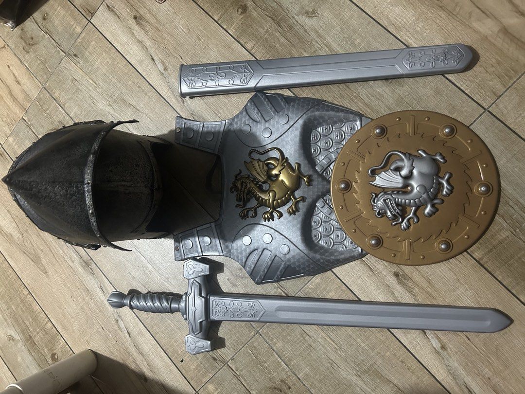 Knight Armor Costume Set Helmet Shield Sword Scabbard (Category: Combat Sports) located in Paranaque City. Submitted by zac.sei (Listing ID 1469804968, Image 3). Description: - Complete medieval knight dress-up set - Includes textured dark grey helmet with visor slits - Silver chest armor featuring a gold dragon emblem - Round gold and silver shield with dragon motif - Long silver sword with matching scabbard - Durable plastic construction - Idea