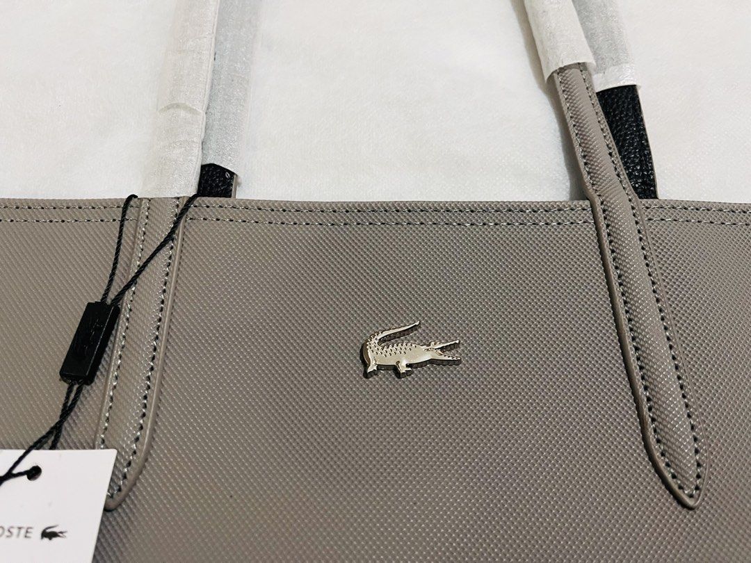 Lacoste Tote Bag Grey (Category: Tote Bags) located in Quezon City. Submitted by pickleballpaddle (Listing ID 1469800363, Image 3). Description: - 100% Authentic Lacoste tote bag in versatile grey - Contrasting black interior with matching handles - Features iconic metal crocodile logo on the front - Includes a matching inner zipped pouch for organization - Brand new with original store tags attached - Handles are wrapped in protective packaging 