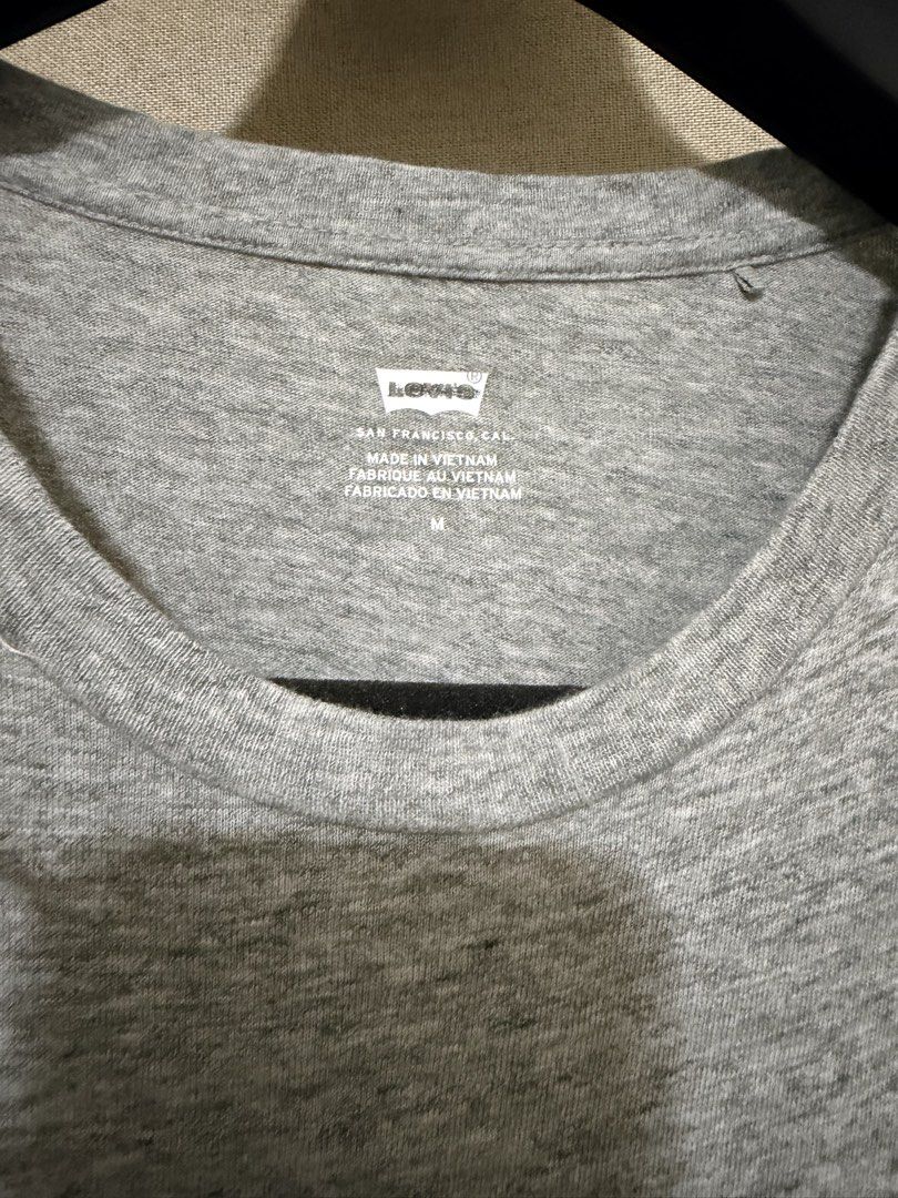 Levi's Grey Logo T-Shirt Size M (Category: Shirts) located in Cavite. Submitted by mgd.blessed (Listing ID 1469905826, Image 2). Description: - Brand: Levi's - Color: Grey with dark blue lettering - Size: Medium (Regular Fit) - Material: Soft cotton blend - Style: Classic crew neck - Condition: Clean overall, ready to wear, with a small hole near the right shoulder seam as pictured.