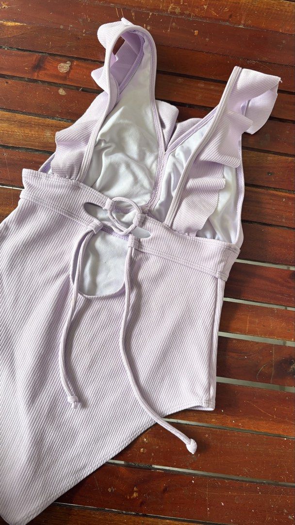 Lilac Ruffle One-Piece Swimsuit (Category: Bikinis & Swimsuits) located in Batangas. Submitted by rachelmaloles (Listing ID 1469769514, Image 2). Description: - Color: Beautiful lilac - Fabric: Premium ribbed, stretchy, and fully lined in white - Design: Plunging neckline with playful ruffle details - Back: Trendy cutout with adjustable lace-up ties for a custom fit - Comfort: Super comfortable, perfect for the beach or pool - Condition: Brand ne