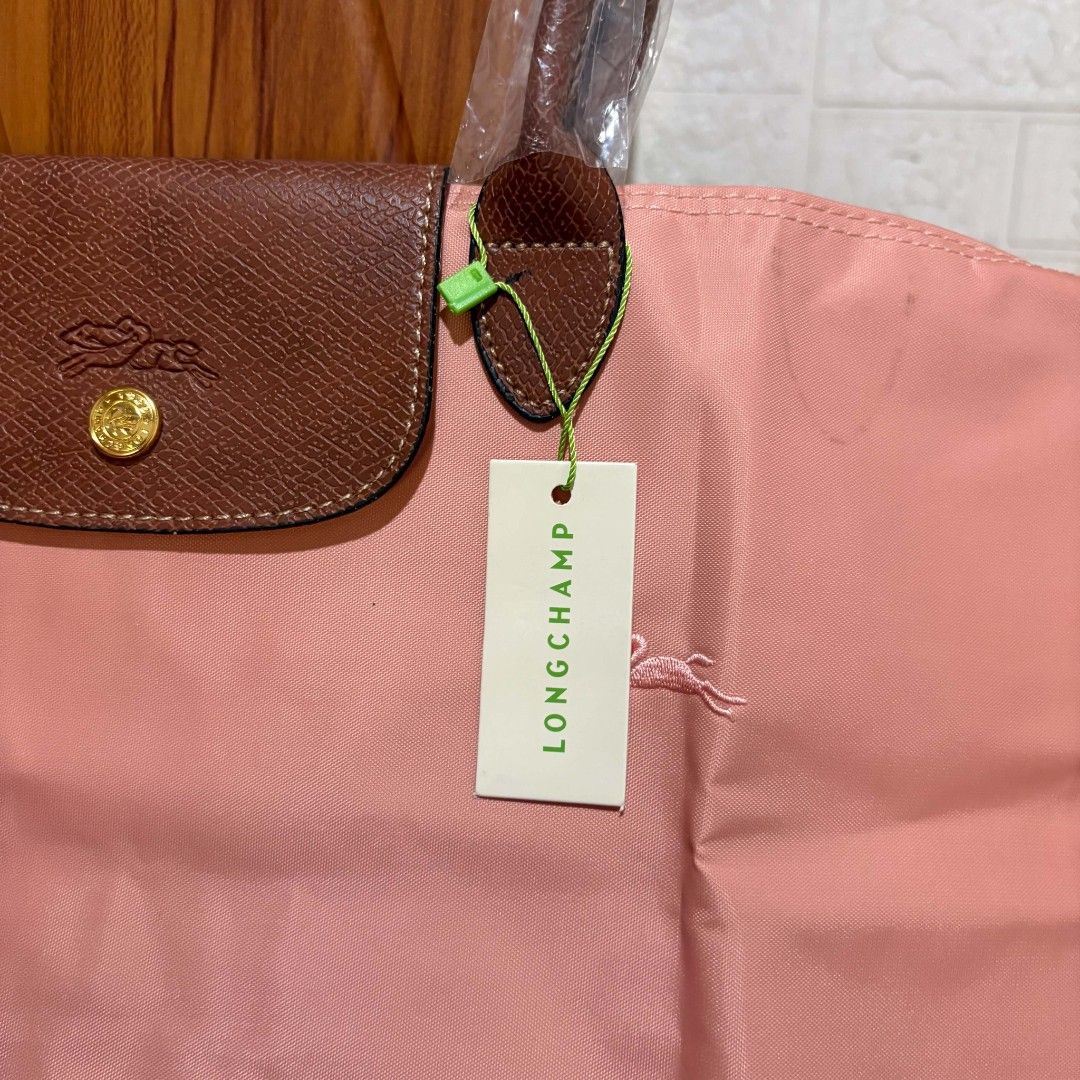 Longchamp Le Pliage Pink Tote Bag (Category: Tote Bags) located in Carmen. Submitted by ar_thrift00 (Listing ID 1469762979, Image 3). Description: - Longchamp Le Pliage Tote Bag in a gorgeous pink shade - Premium brown leather top flap with snap closure and gold-tone hardware - Durable, clean nylon body with the signature embroidered horse logo - Interior white tag indicates 'Made in France' with official product codes - Spacious, lightweight, an