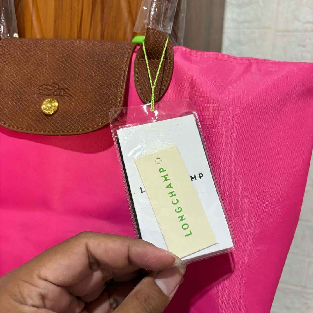 Longchamp Paris Pink Nylon Handbag (Category: Tote Bags) located in Carmen. Submitted by ar_thrift00 (Listing ID 1469762938, Image 3). Description: - Longchamp Paris handbag made in France - Eye-catching bright pink nylon body with clean interior - Classic brown leather flap featuring a gold-tone snap button closure - Gold zipper pull accented with the iconic jockey logo and 1948 branding - White interior lining complete with authenticity codes (