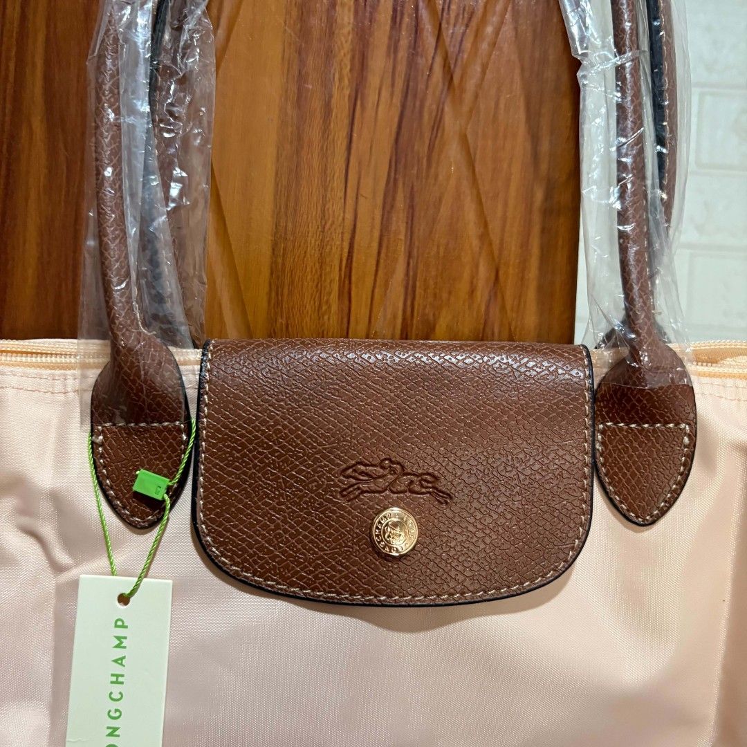 Longchamp Paris Tote Bag Beige Brown (Category: Tote Bags) located in Carmen. Submitted by ar_thrift00 (Listing ID 1469762791, Image 3). Description: - Brand: Longchamp Paris (Made in France) - Condition: Brand new, never used (Plastic wrapping still on handles) - Color: Beige nylon body with brown leather flap and handles - Features: Secure zip closure, snap button flap, and inner - as is.