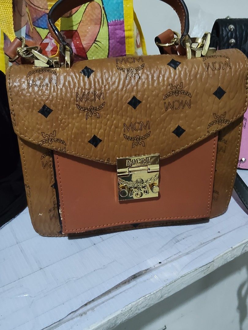 MCM Brown Leather Top Handle Shoulder Bag (Category: Luxury Bags & Wallets) located in Cebu City. Submitted by almzcorner (Listing ID 1469922805, Image 1). Description: - Brand: MCM - Material: Brown pebbled leather with signature monogram pattern - Details: Solid brown front pocket & gold-tone hardware with engraved branding - Interior: Red fabric lining with a zippered pocket and brand plaque - Inclusion: Matching adjustable shoulder strap incl